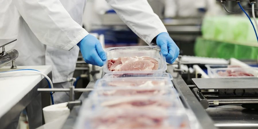Close up of a meat industry worker gathering packed meat on a conveyor belt.